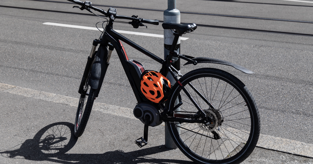 Elektrische fiets met een oranje helm staat tegen een lantaarnpaal aan