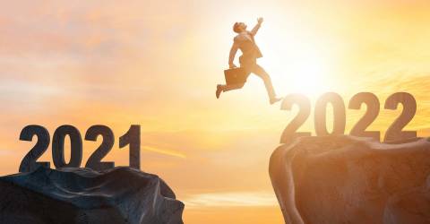 Zakenman springt van een rots met 2021 naar een rost met 2022 met op de achtergrond zon